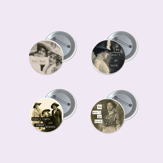Four round pinback buttons with vintage-style black and white historical photographs and text slogans, shown with their silver metal backs on a pale lavender background.