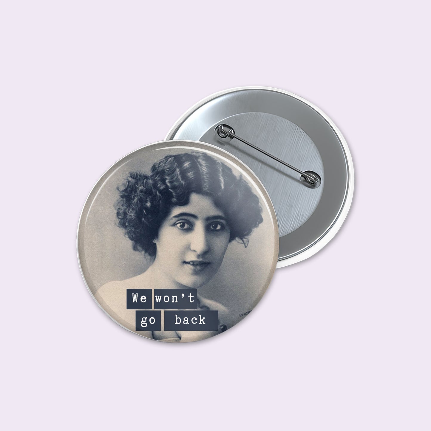 Round pinback button shows a vintage black-and-white portrait of a woman with the text 'We won't go back' in dark blocks.