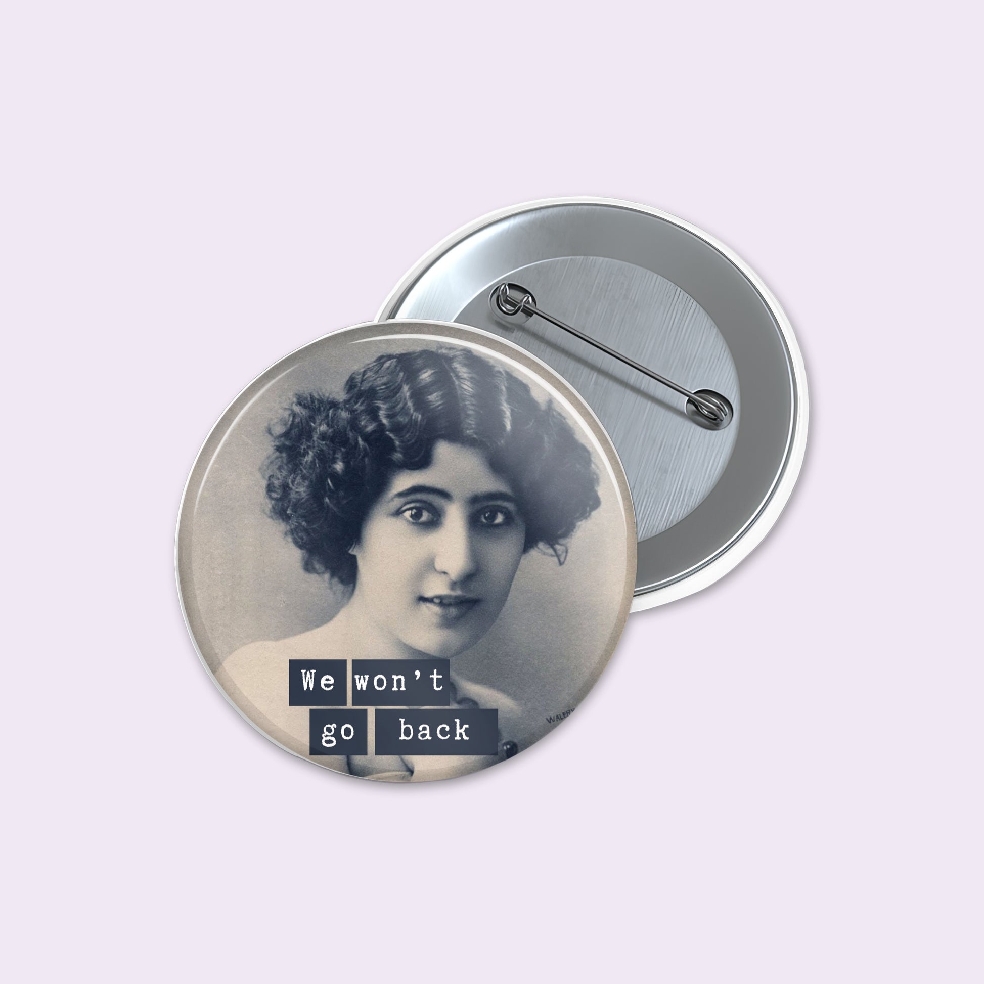 Round pinback button shows a vintage black-and-white portrait of a woman with the text 'We won't go back' in dark blocks.
