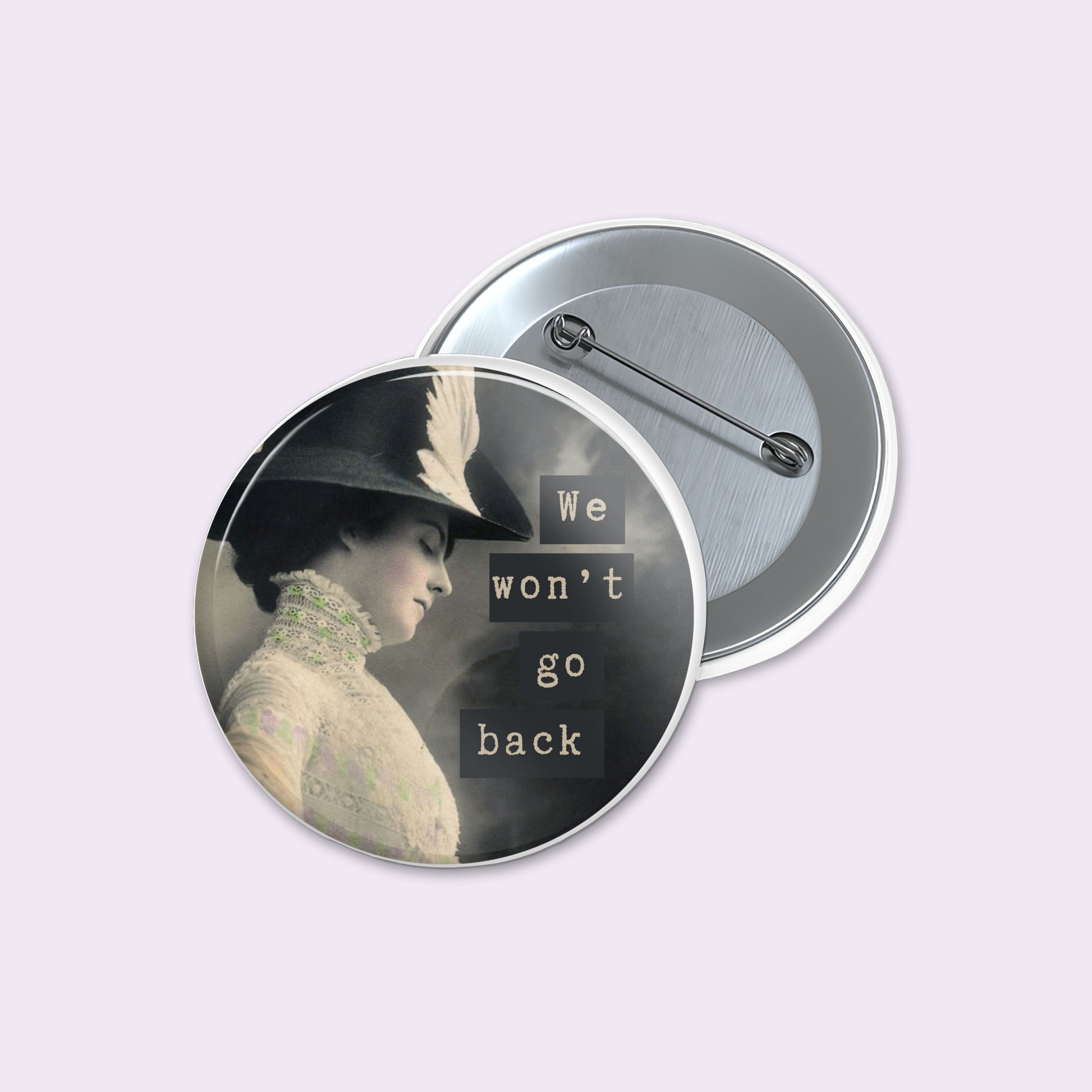 Round pinback button shows a vintage-style portrait of a woman in profile wearing a feathered hat, with the text 'We won't go back' in white lettering.