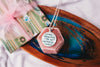 Necklace with a pendant featuring an upcycled book page on a wooden tray with a colorful box in the background