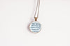 Close-up of round glass pendant showing printed book text set under a glass cabochon and into a bronze-plated bezel