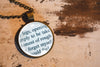 Close-up of round glass pendant showing printed book text set under a glass cabochon and into a bronze-plated bezel