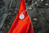 Close-up of a black jacket with a red shirt underneath, featuring a necklace with a round pendant containing an upcycled book page.