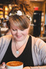 Woman with floral hair accessory and wearing a pendant necklace with upcycled book page pendant displaying text  holding a cup in a casual setting