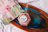 Upcycled book page pendant necklace with pendant featuring book page text, on a pink velvet jewelry box on a colorful tray