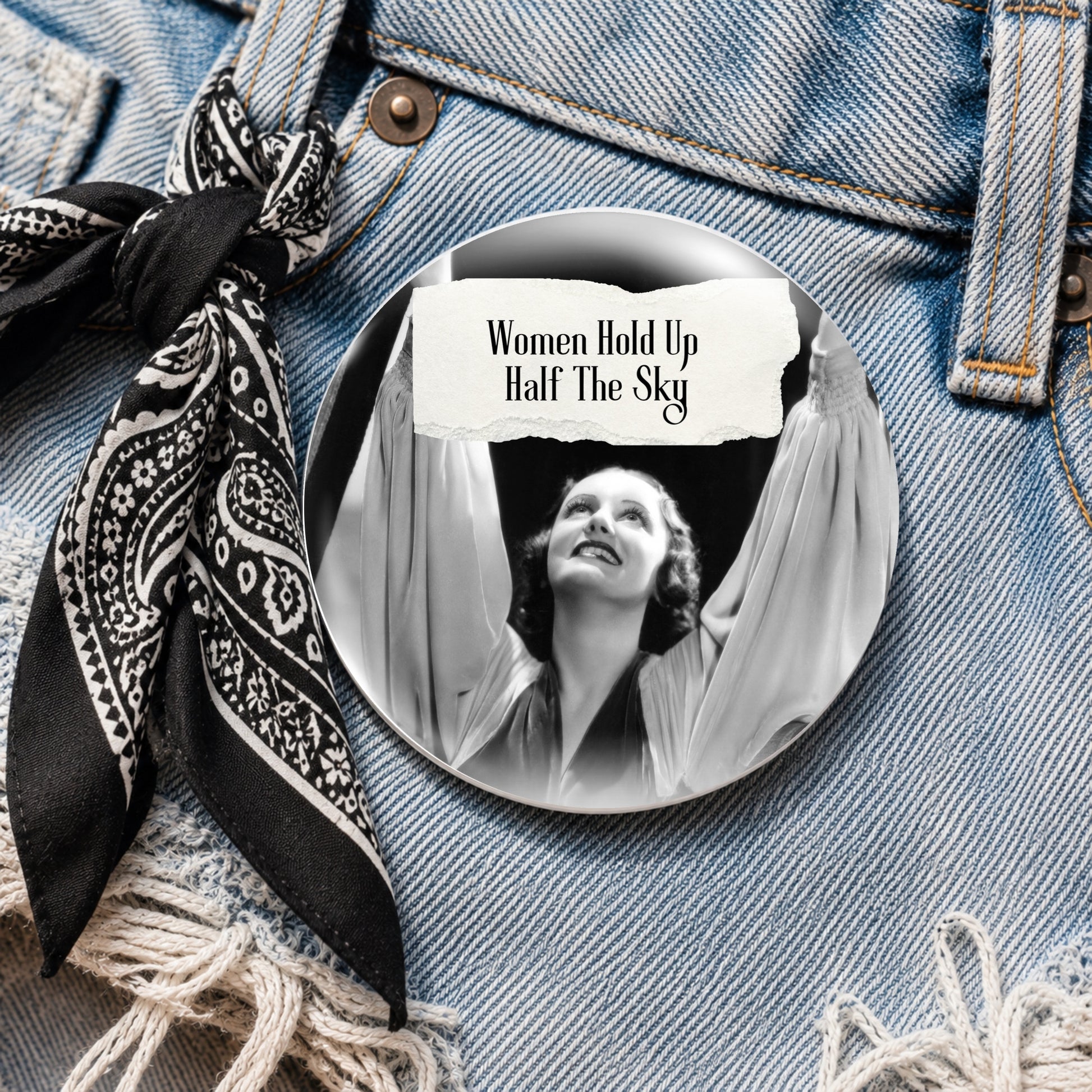 Feral retro woman pin back button with quote that says "Women Hold Up Half The Sky" shown on denim 