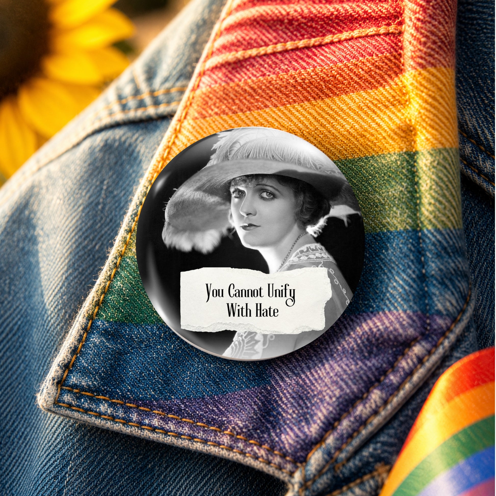 A round pin-back button badge featuring a black-and-white portrait of a woman in a hat with the text 'You Cannot Unify With Hate,' placed on a denim jacket with a rainbow-striped fabric accent.