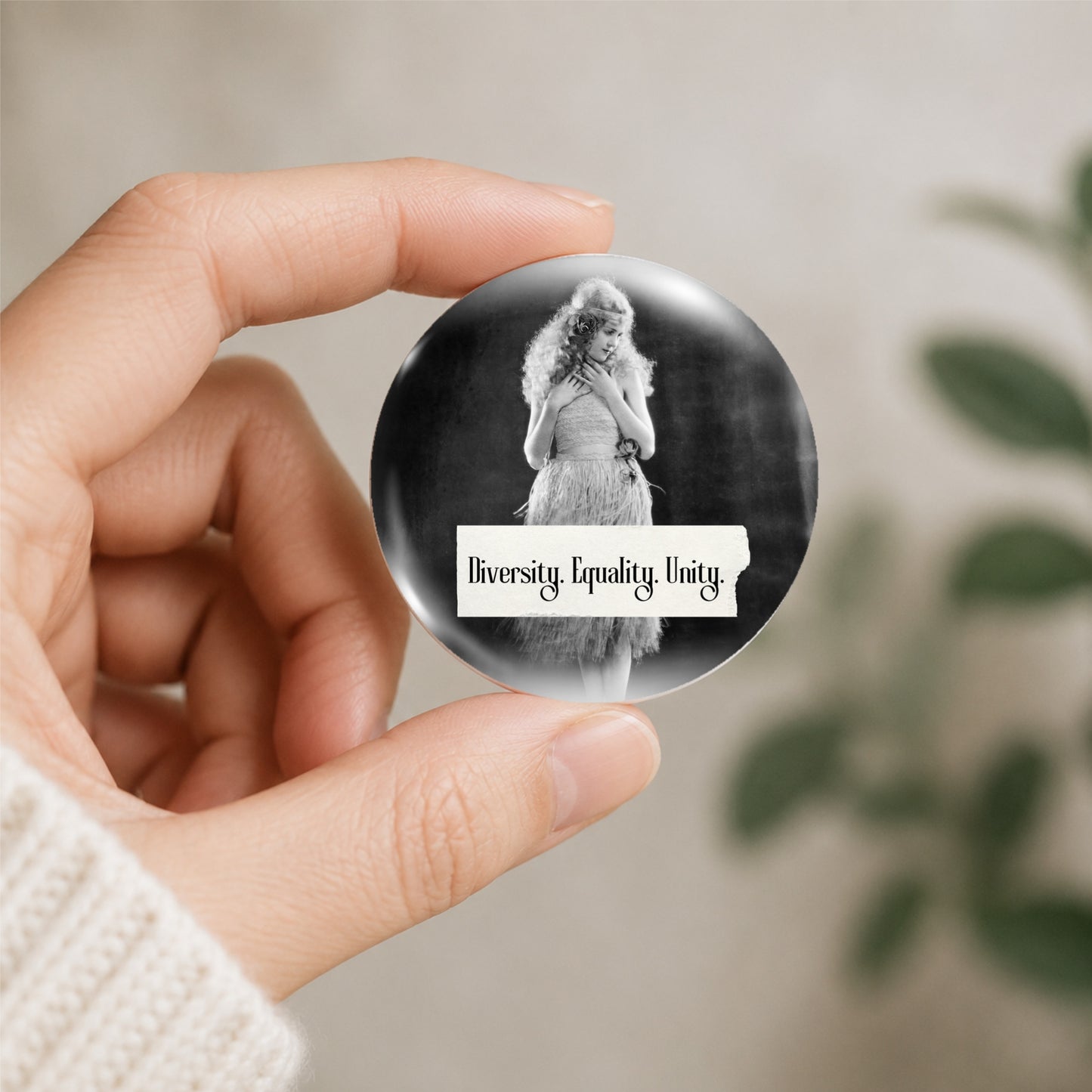 Retro woman on a pin back button with writing "Diversity. Equality. Unity." shown being held