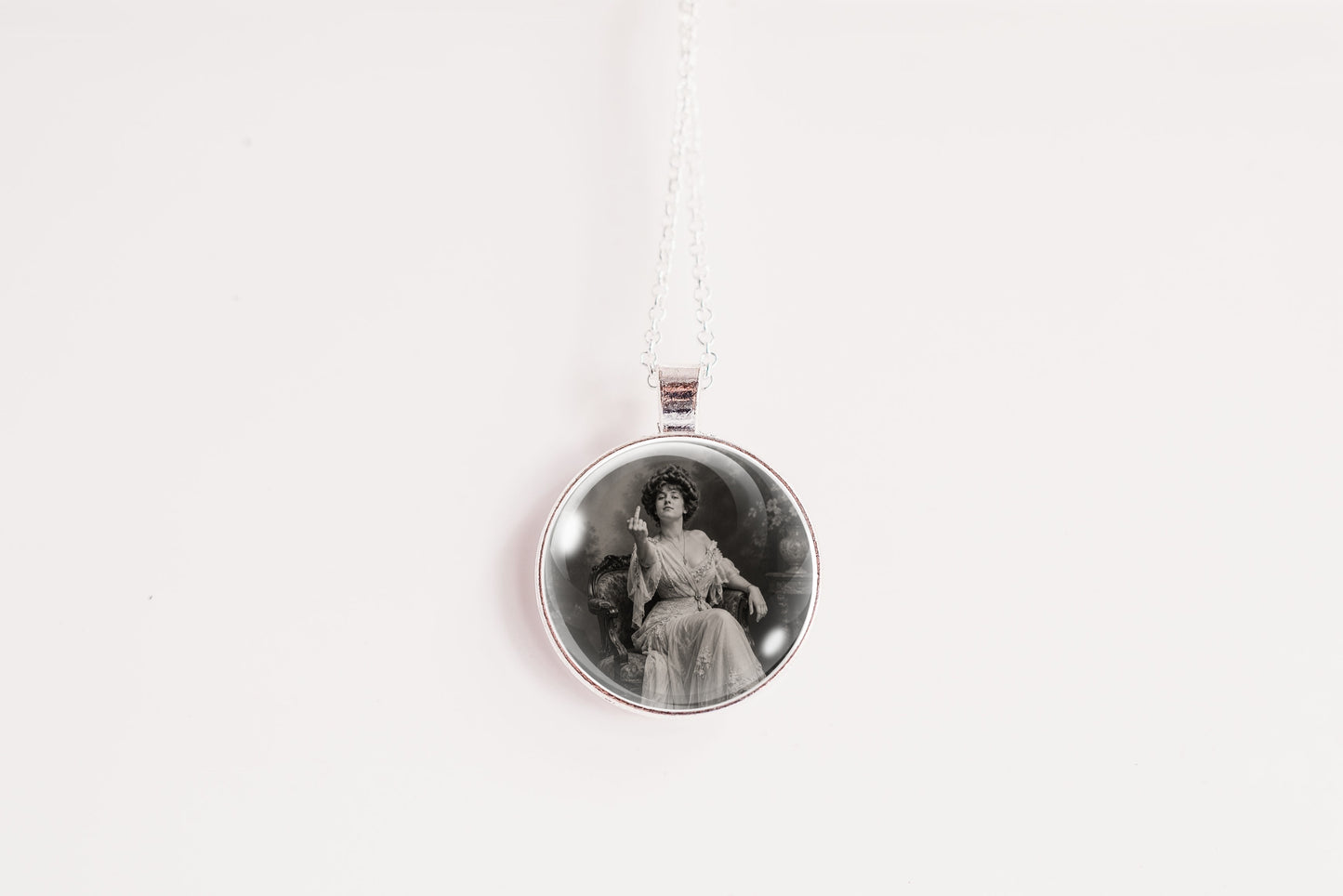 A silver-toned circular pendant necklace featuring a black and white vintage portrait of a seated woman, suspended from a thin silver chain against a plain white background.