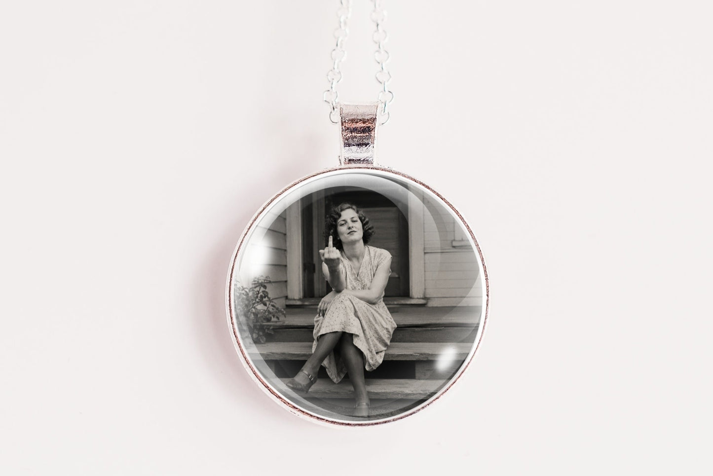 A silver round pendant necklace featuring a black and white photograph of a woman sitting on steps, suspended from a silver chain against a plain white background.