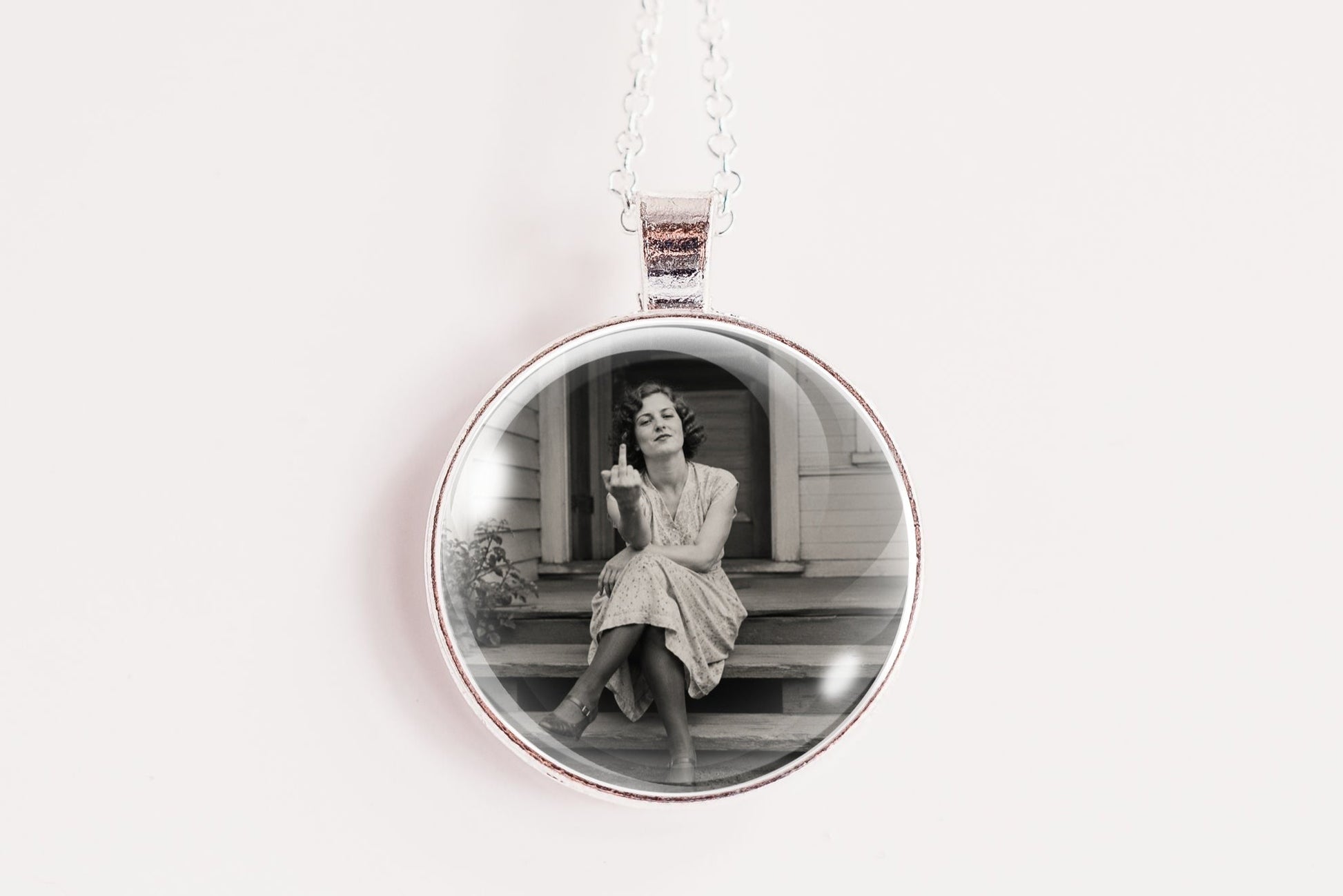 A silver round pendant necklace featuring a black and white photograph of a woman sitting on steps, suspended from a silver chain against a plain white background.