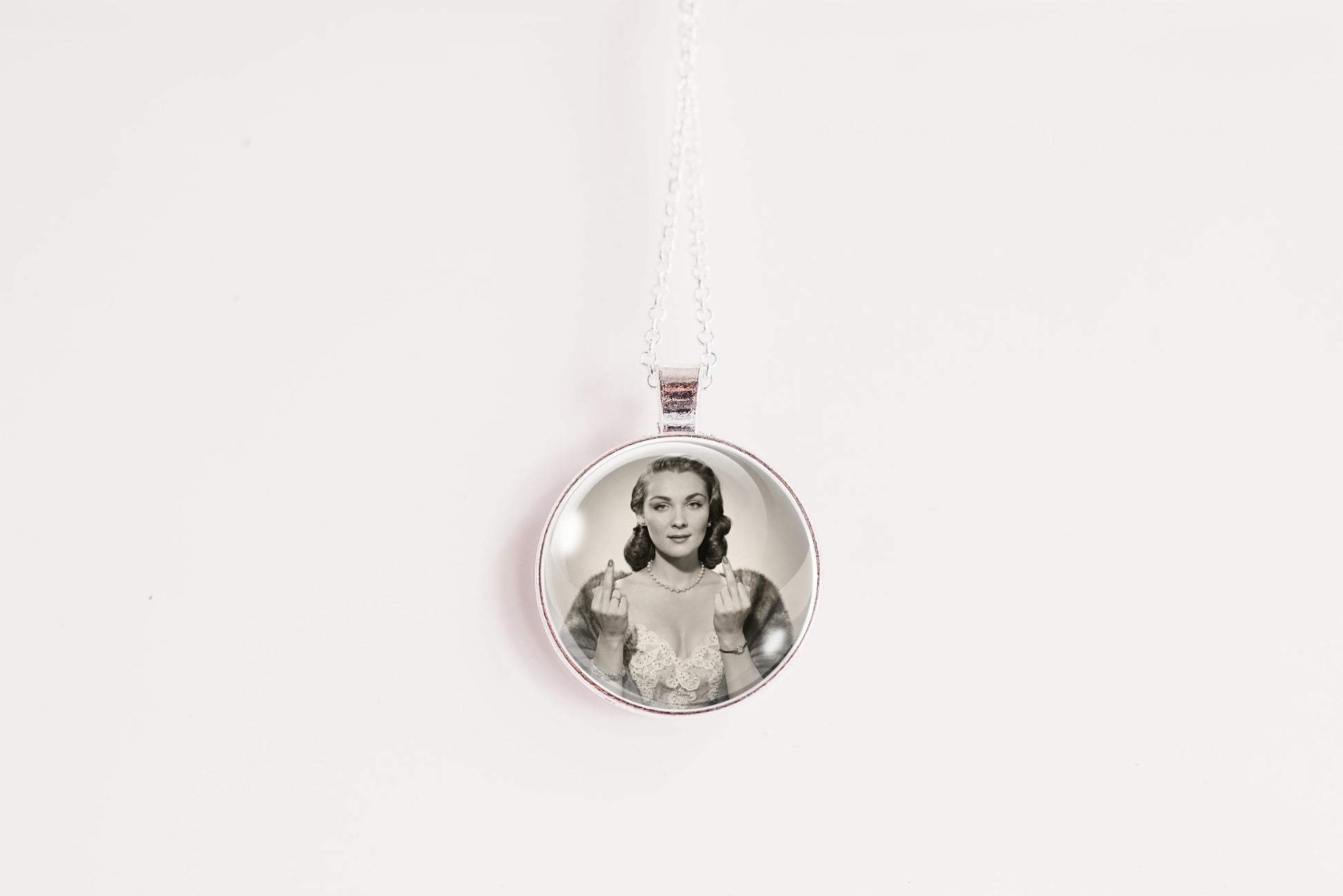 A silver circular pendant necklace featuring a black-and-white portrait photo of a woman, suspended from a white cord against a plain white background.