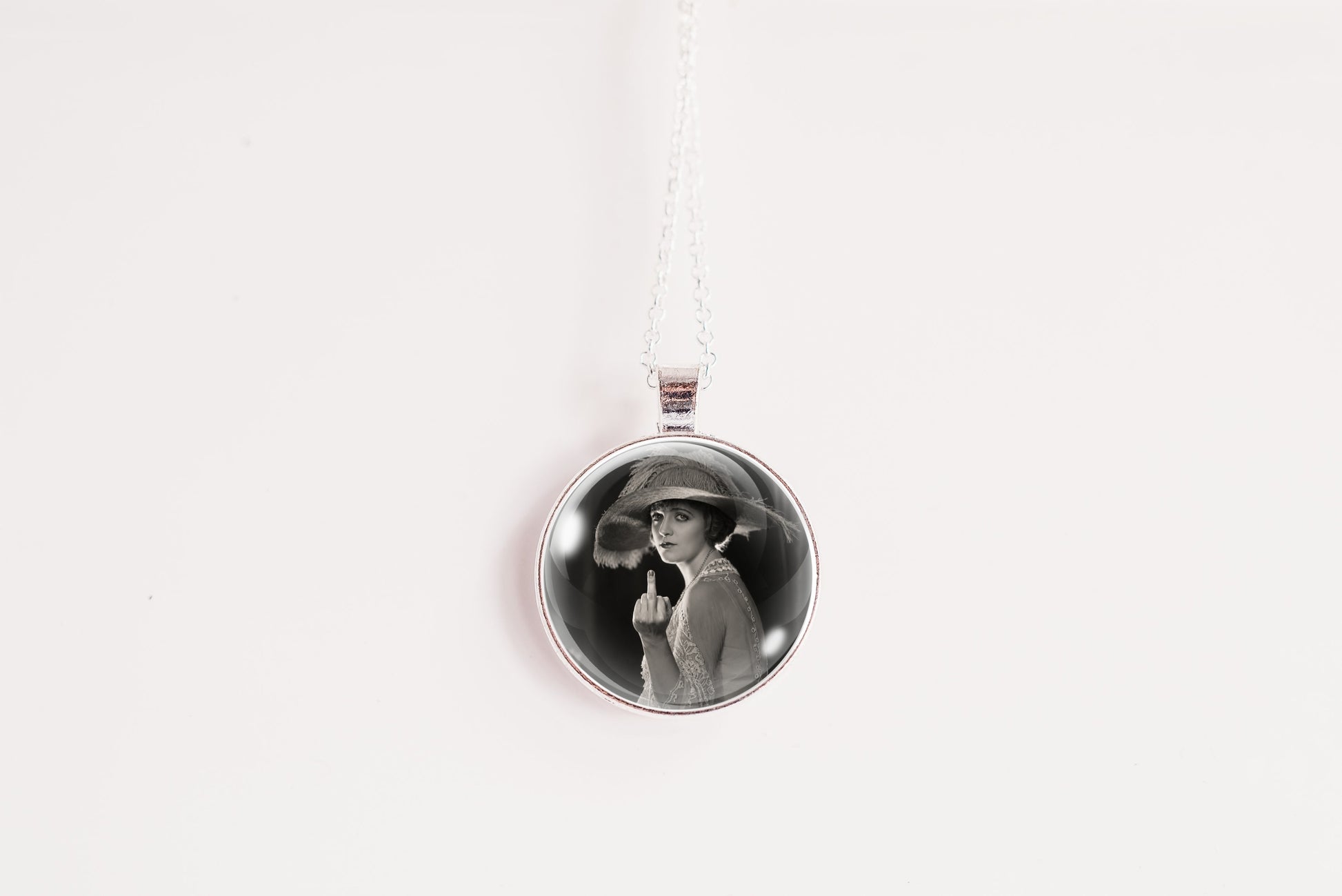 A silver circular pendant necklace featuring a black-and-white portrait photo of a woman in a hat, suspended on a silver chain against a plain white background.