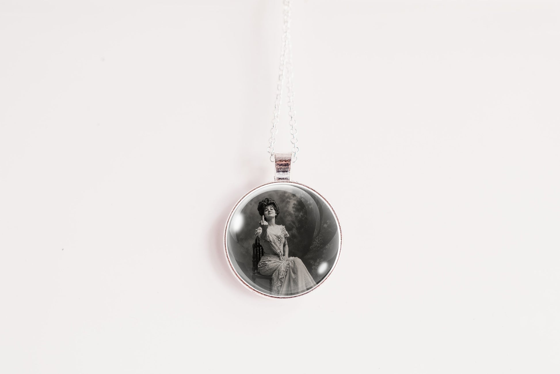A silver circular pendant necklace featuring a black and white vintage portrait of a seated woman, suspended from a thin silver chain against a plain white background.