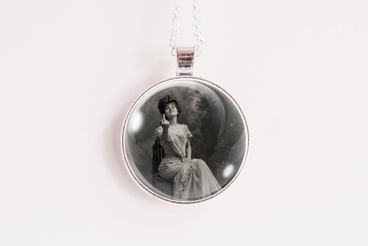 A silver circular pendant necklace featuring a black and white vintage portrait of a seated woman, suspended from a thin silver chain against a plain white background.