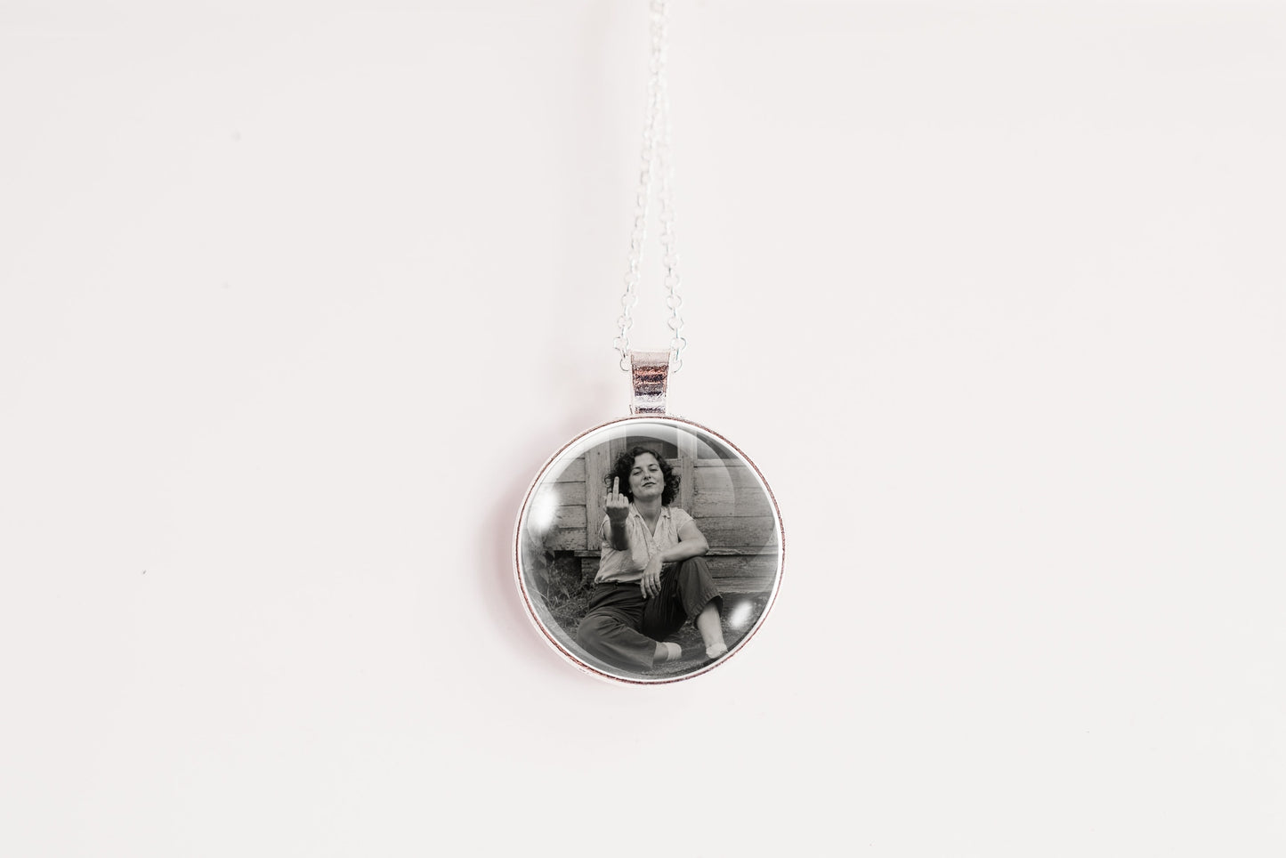 A silver round pendant necklace featuring a black and white photo of a woman sitting on steps, suspended from a white cord against a plain white background.