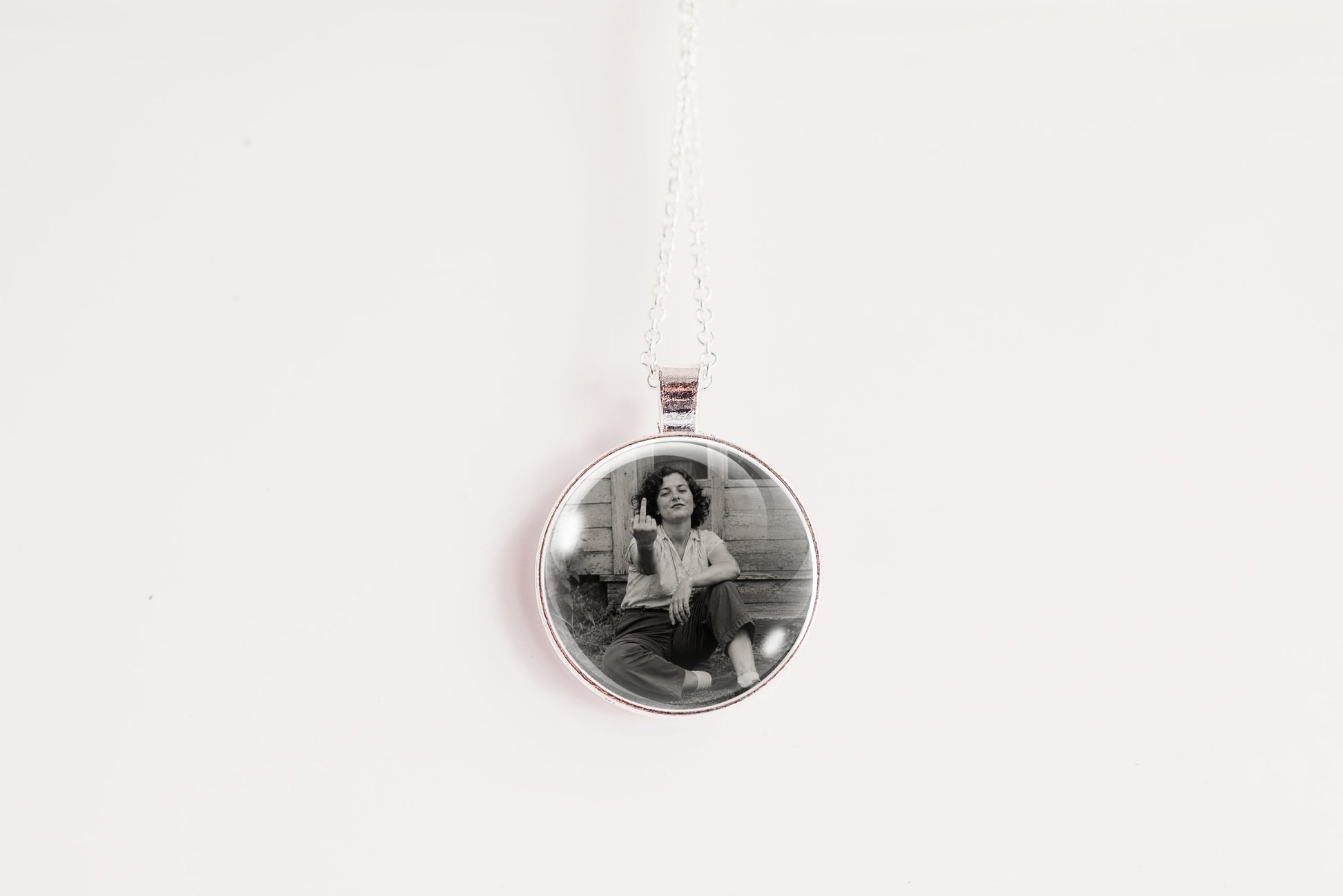 A silver round pendant necklace featuring a black and white photo of a woman sitting on steps, suspended from a white cord against a plain white background.