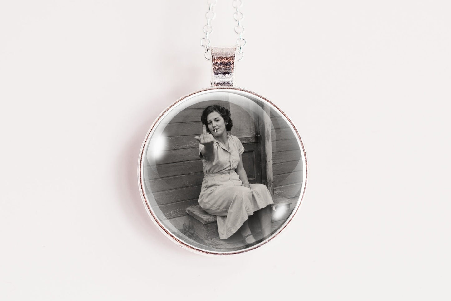 A silver circular pendant necklace featuring a black and white vintage photograph of a woman sitting on steps, suspended from a silver chain against a plain white background.