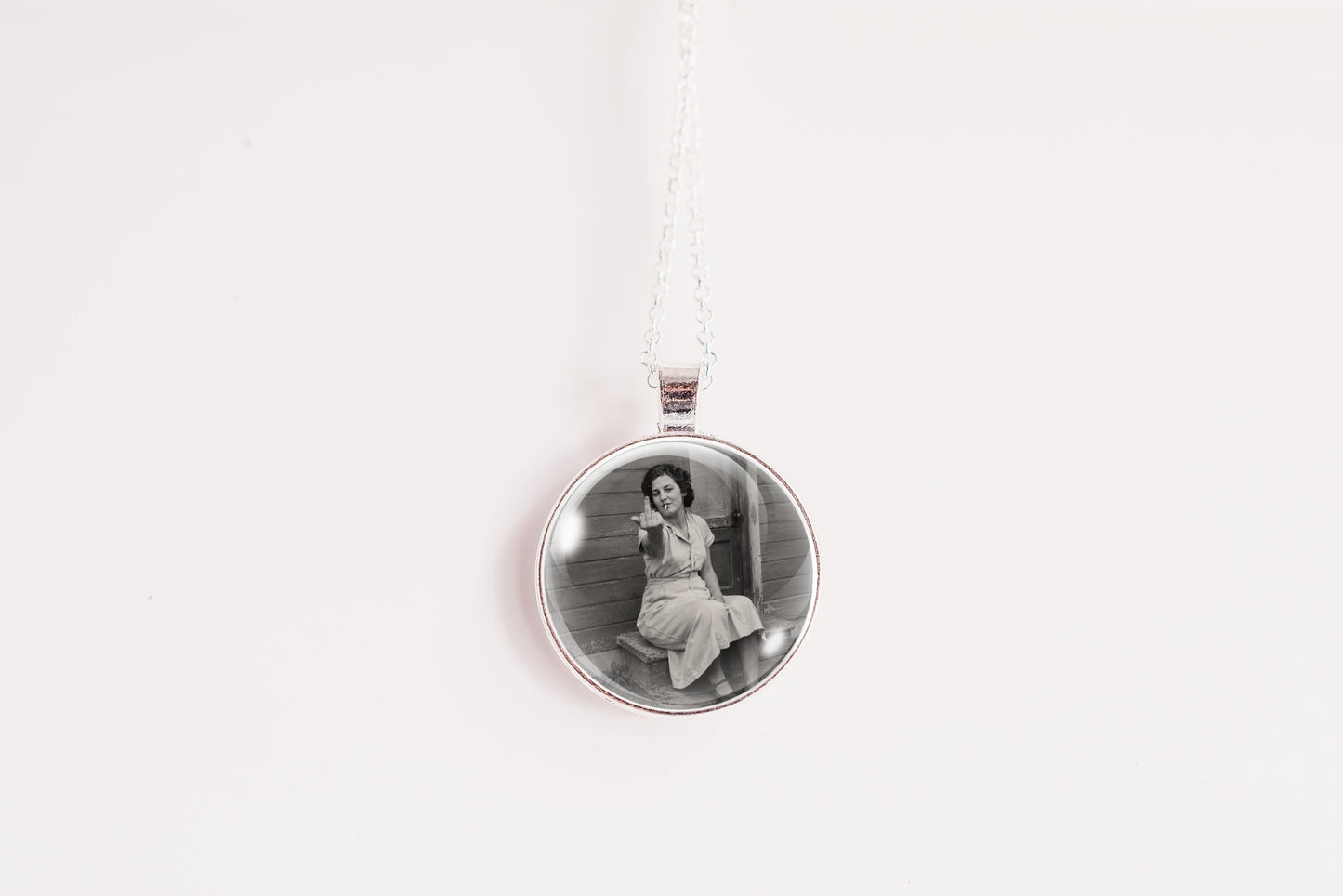 A silver circular pendant necklace featuring a black and white vintage photograph of a woman sitting on steps, suspended from a white cord against a plain white background.
