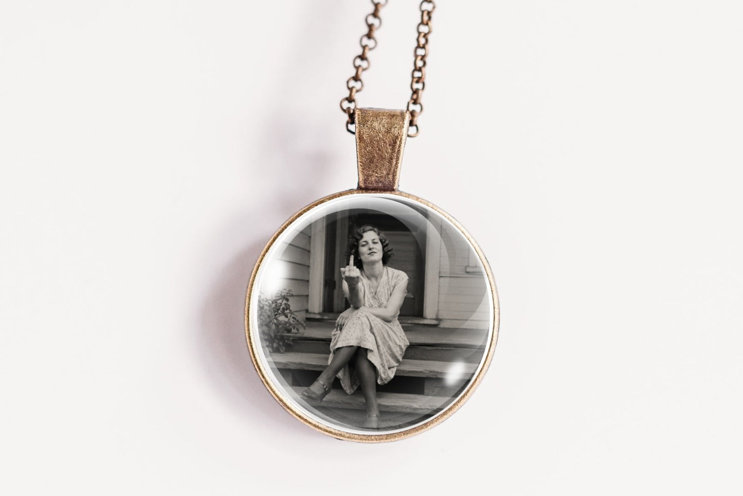 A round pendant necklace featuring a black and white vintage photograph of a woman sitting on steps, suspended from a delicate bronze chain against a plain white background.