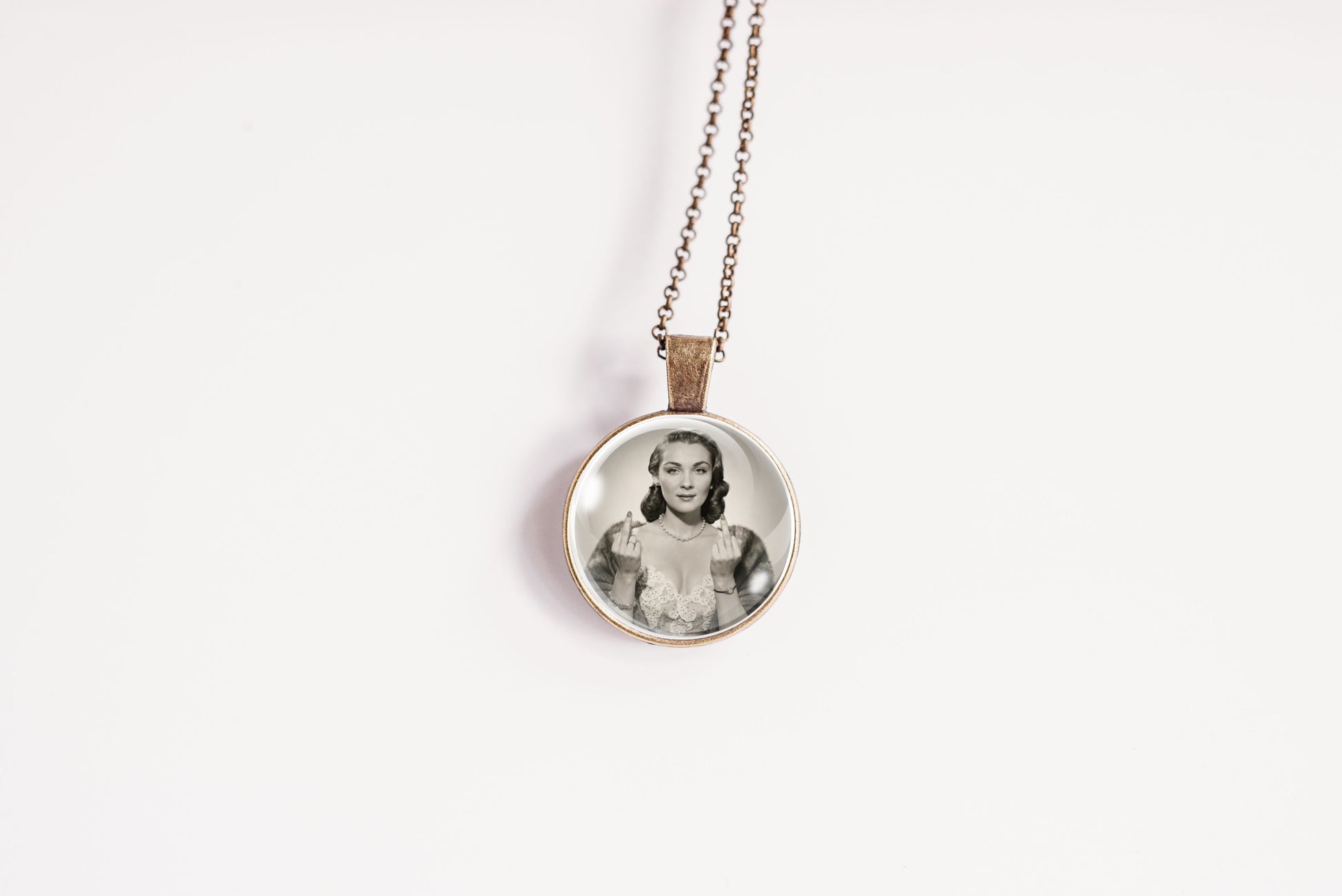 A round pendant necklace featuring a black and white portrait photograph of a woman, suspended from a delicate bronze-toned chain against a plain white background.