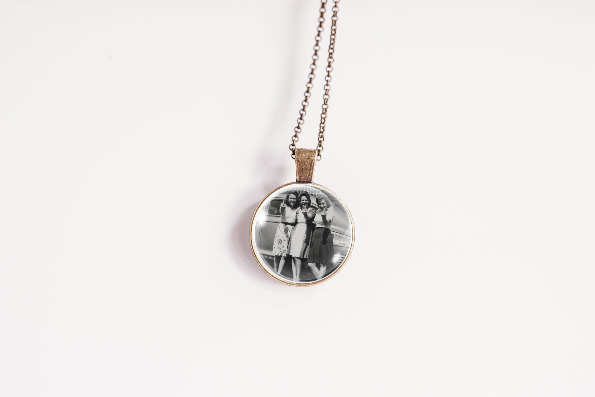 A round pendant necklace featuring a black and white photograph of three women, suspended from a delicate bronze-colored chain against a plain white background.