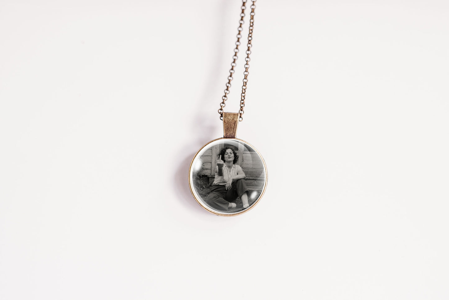 A round pendant necklace featuring a black and white photograph of a woman, suspended from a delicate bronze-colored chain against a plain white background.