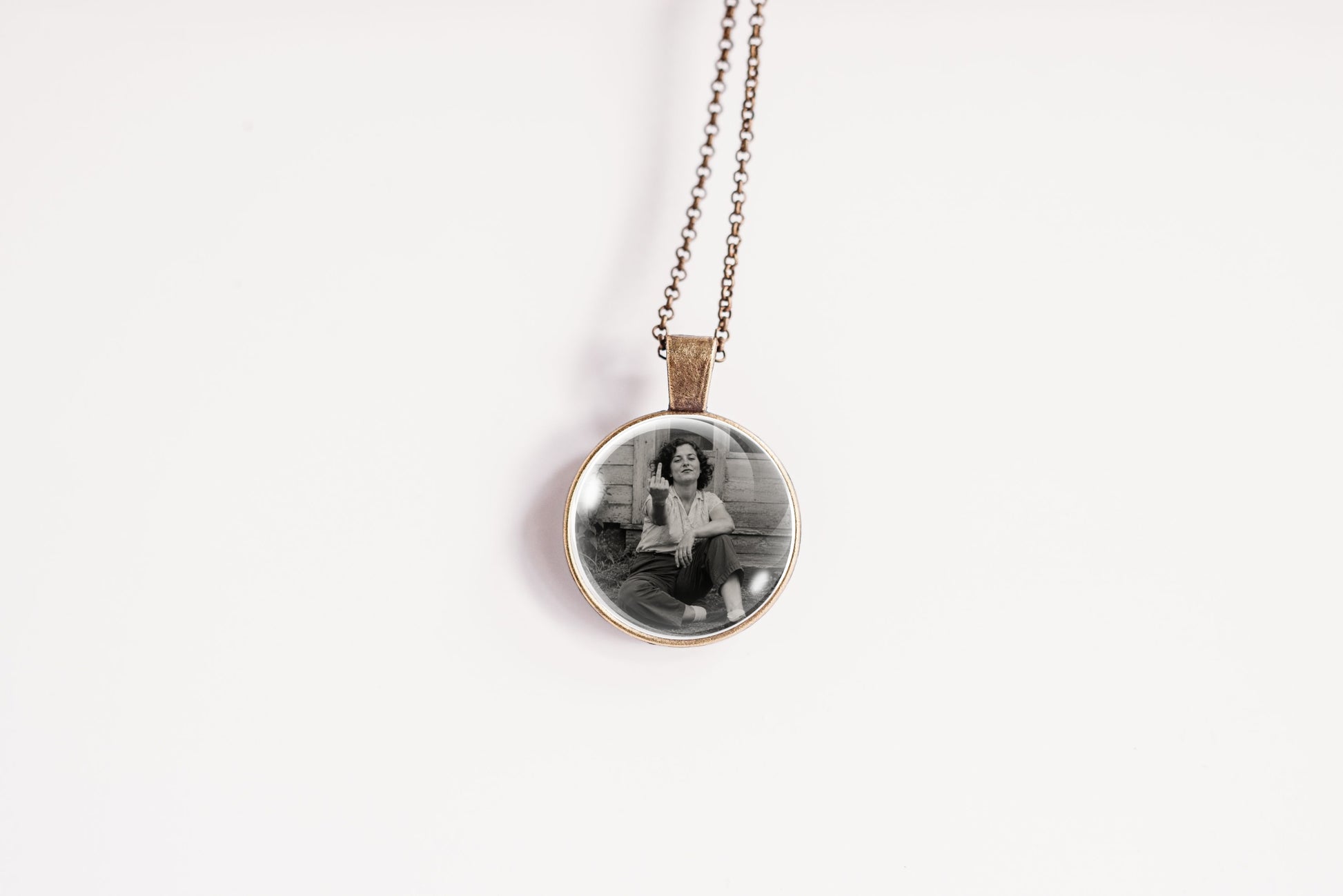 A round pendant necklace featuring a black and white photograph of a woman, suspended from a delicate bronze-colored chain against a plain white background.