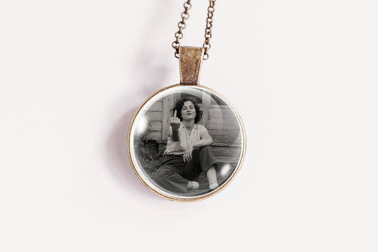 A round pendant necklace featuring a black and white photograph of a woman, suspended from a delicate bronze-colored chain against a plain white background.
