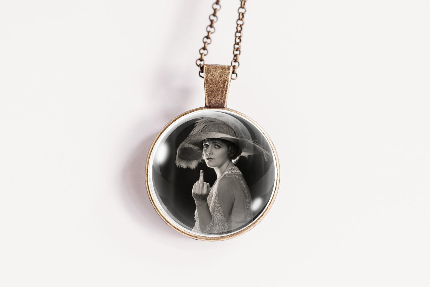 A round pendant necklace featuring a black and white portrait photograph of a woman in a hat, suspended from a delicate bronze-toned chain against a plain white background.