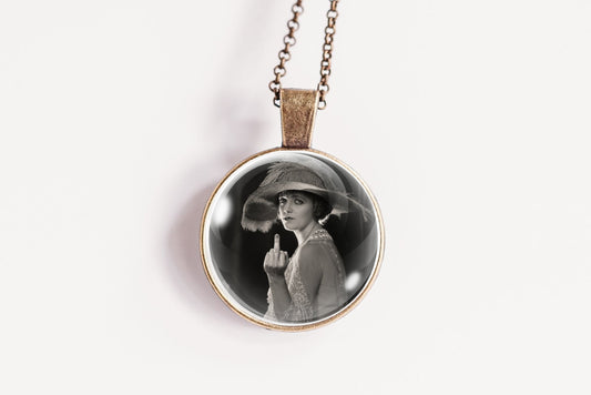 A round pendant necklace featuring a black and white portrait photograph of a woman in a hat, suspended from a delicate bronze-toned chain against a plain white background.