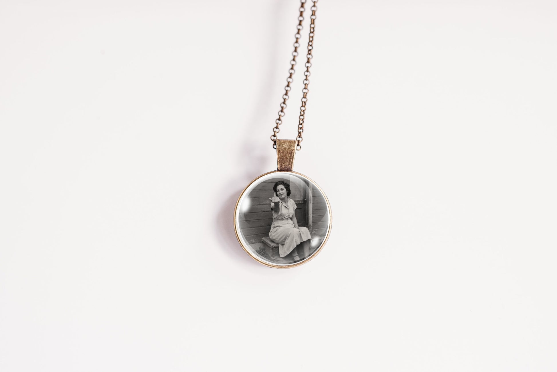 A round pendant necklace featuring a black and white vintage portrait of a seated woman, suspended from a delicate chain against a plain white background.
