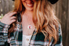 Person wearing a plaid shirt with a floral necklace and a hat, against a blurred background