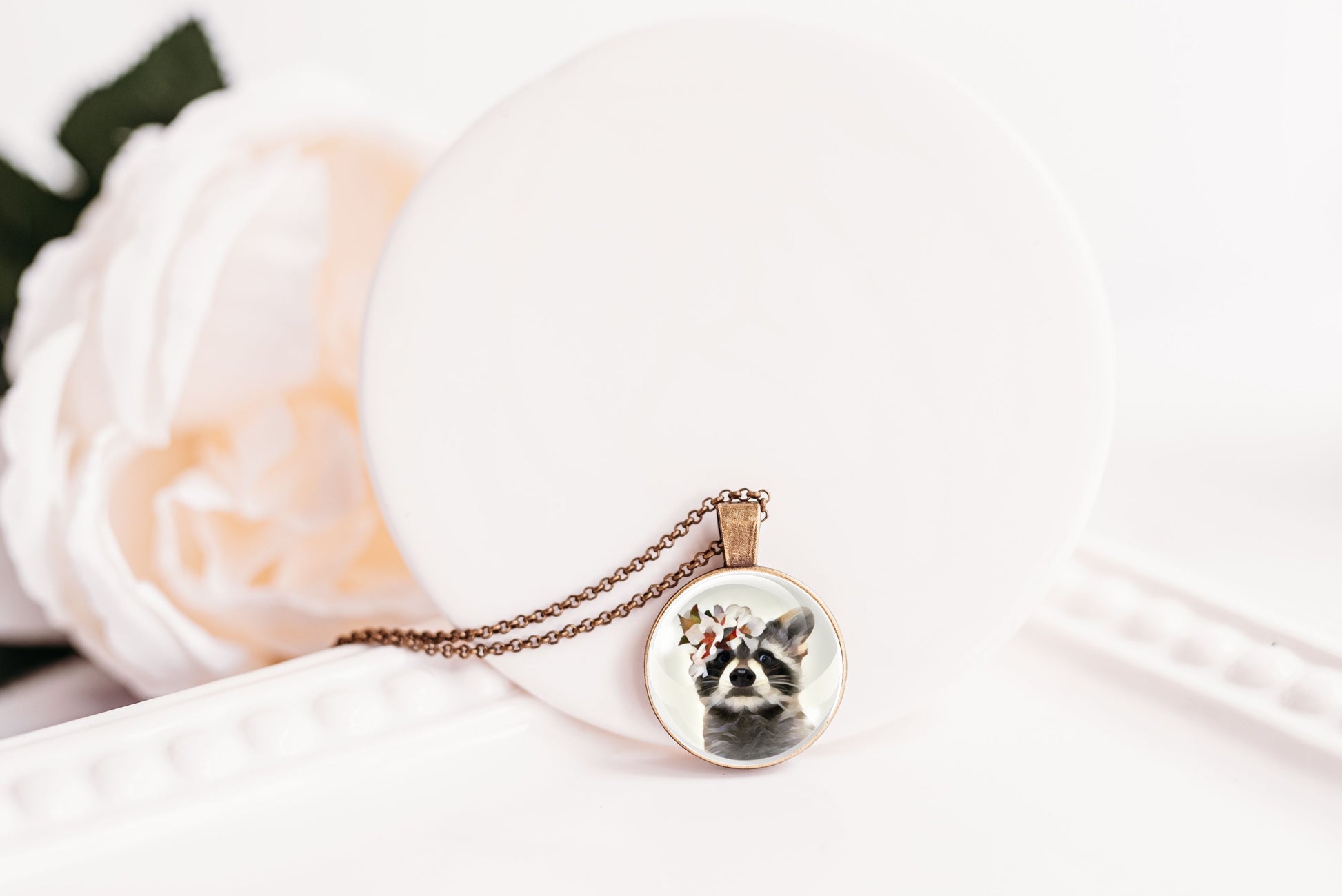 Necklace with a pendant featuring a raccoon wearing a flower crown shown against a white background
