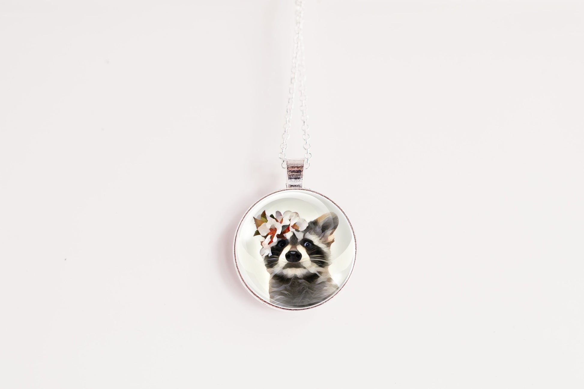 Necklace with a pendant featuring a raccoon wearing a flower crown shown against a white background