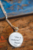 Necklace with an upcycled book page pendant featuring text on a wooden surface
