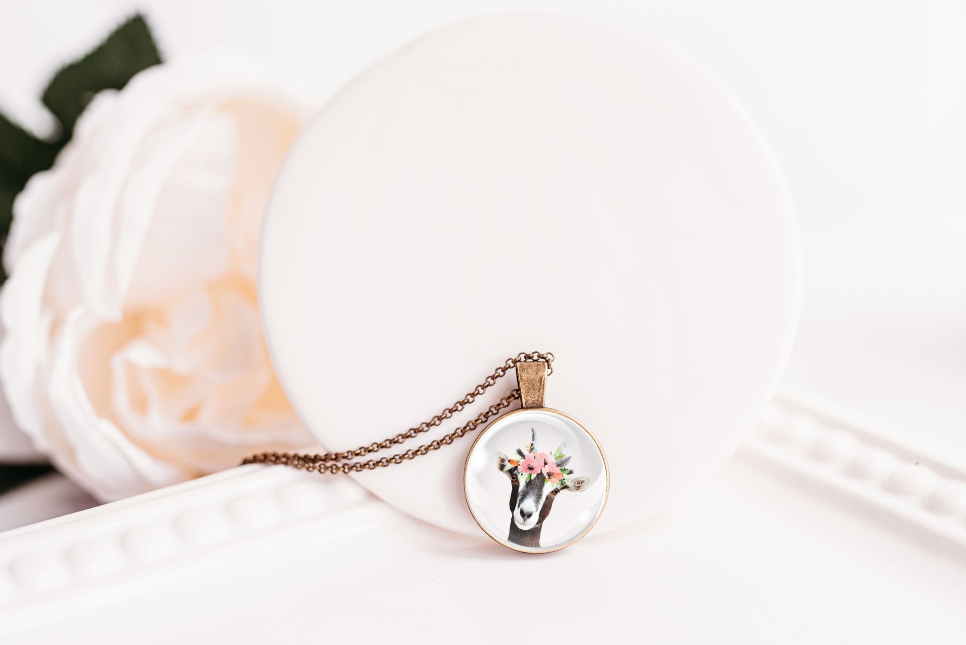 Pendant necklace featuring the image of a goat wearing a flower crown, on a white background