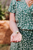 Woman holding a necklace with a round highland cow pendant in their hand, wearing a green floral dress.