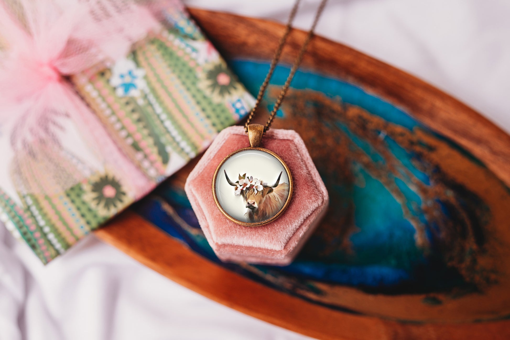Highland cow pendant necklace on a a pink velvet box on a colorful tray
