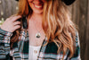Person wearing a plaid shirt, an otter necklace, and a black hat with a blurred background