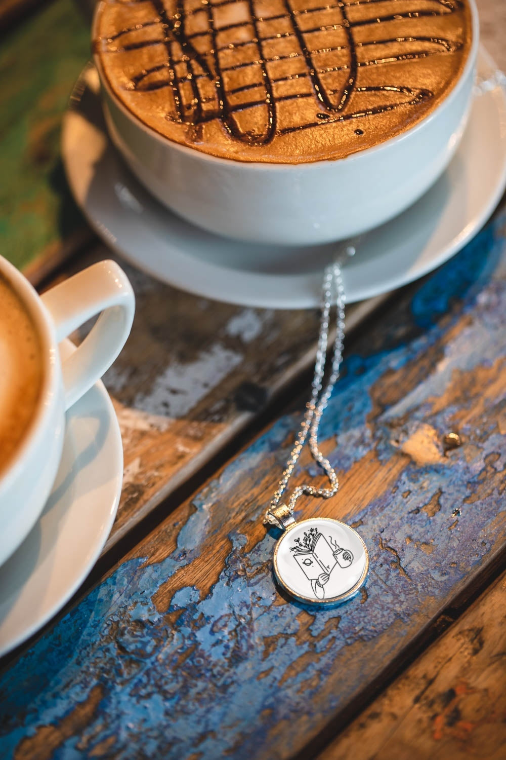 Cup of coffee with a bookish image pendant necklace on a wooden surface