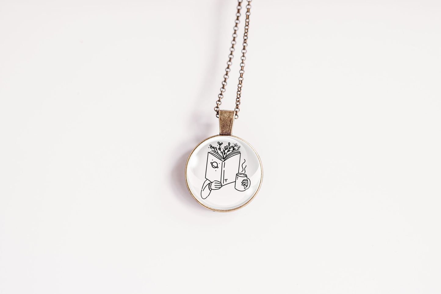 Necklace with a bronze-plated pendant featuring an image of a hand holding a book with branches coming out of the top and a cup, on a white background