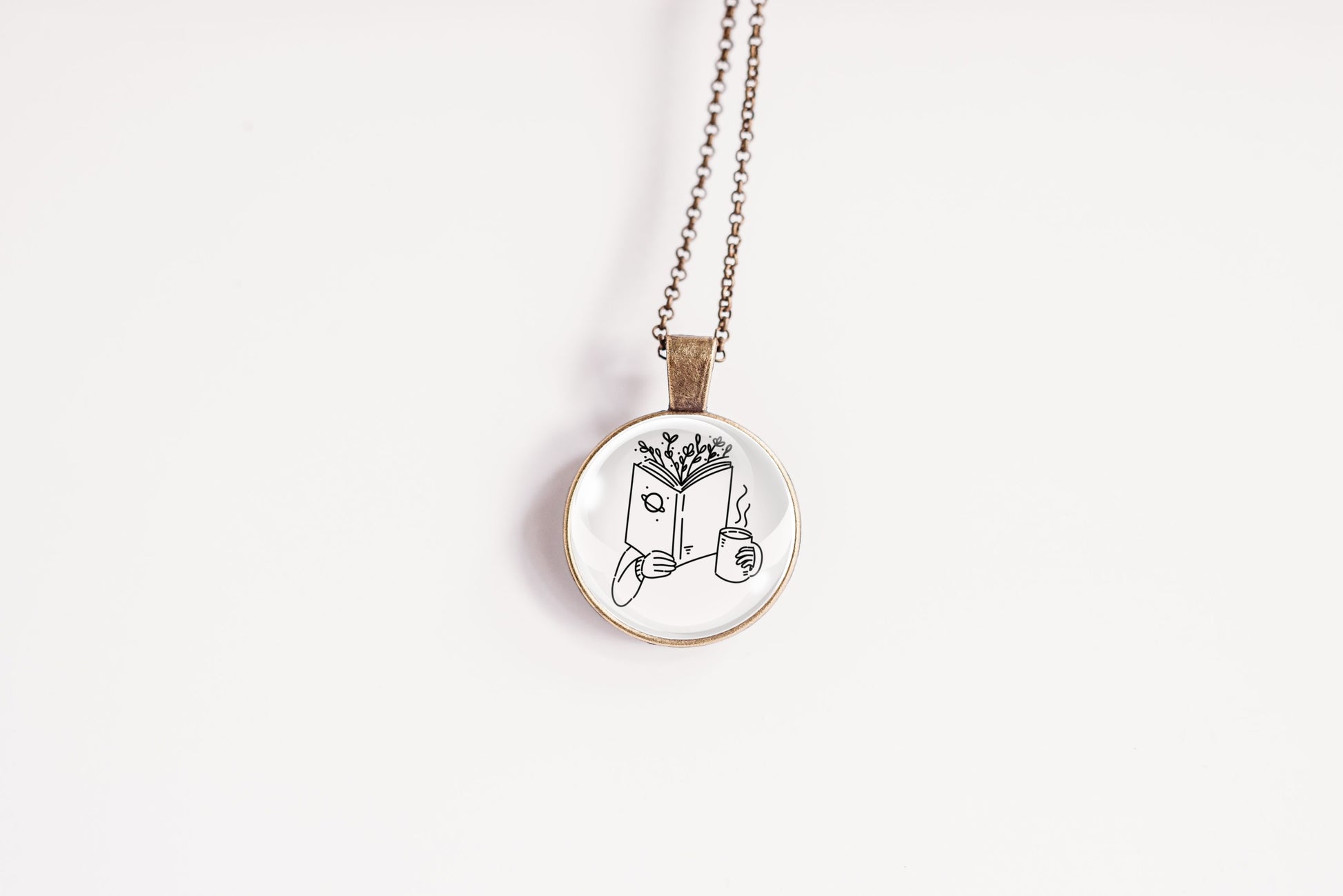 Necklace with a bronze-plated pendant featuring an image of a hand holding a book with branches coming out of the top and a cup, on a white background