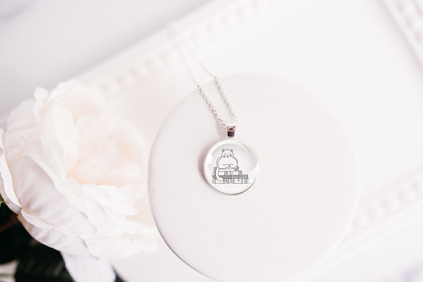 Glass cabochon pendant featuring a black line drawing of a cat sitting on stacked books