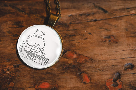 Glass cabochon pendant featuring a black line drawing of a cat sitting on stacked books