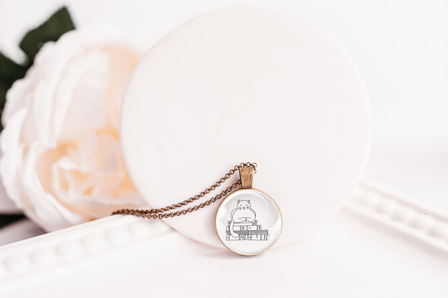 Glass cabochon pendant featuring a black line drawing of a cat sitting on stacked books