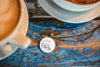 Necklace with a pendant on a wooden surface next to a cup of coffee