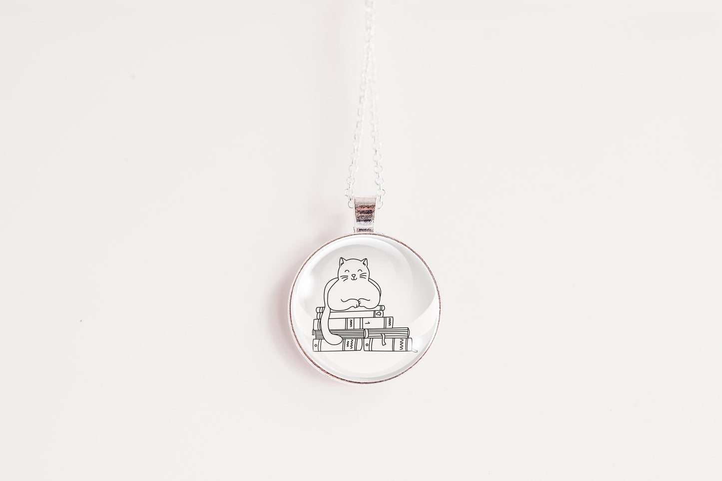 Glass cabochon pendant featuring a black line drawing of a cat sitting on stacked books
