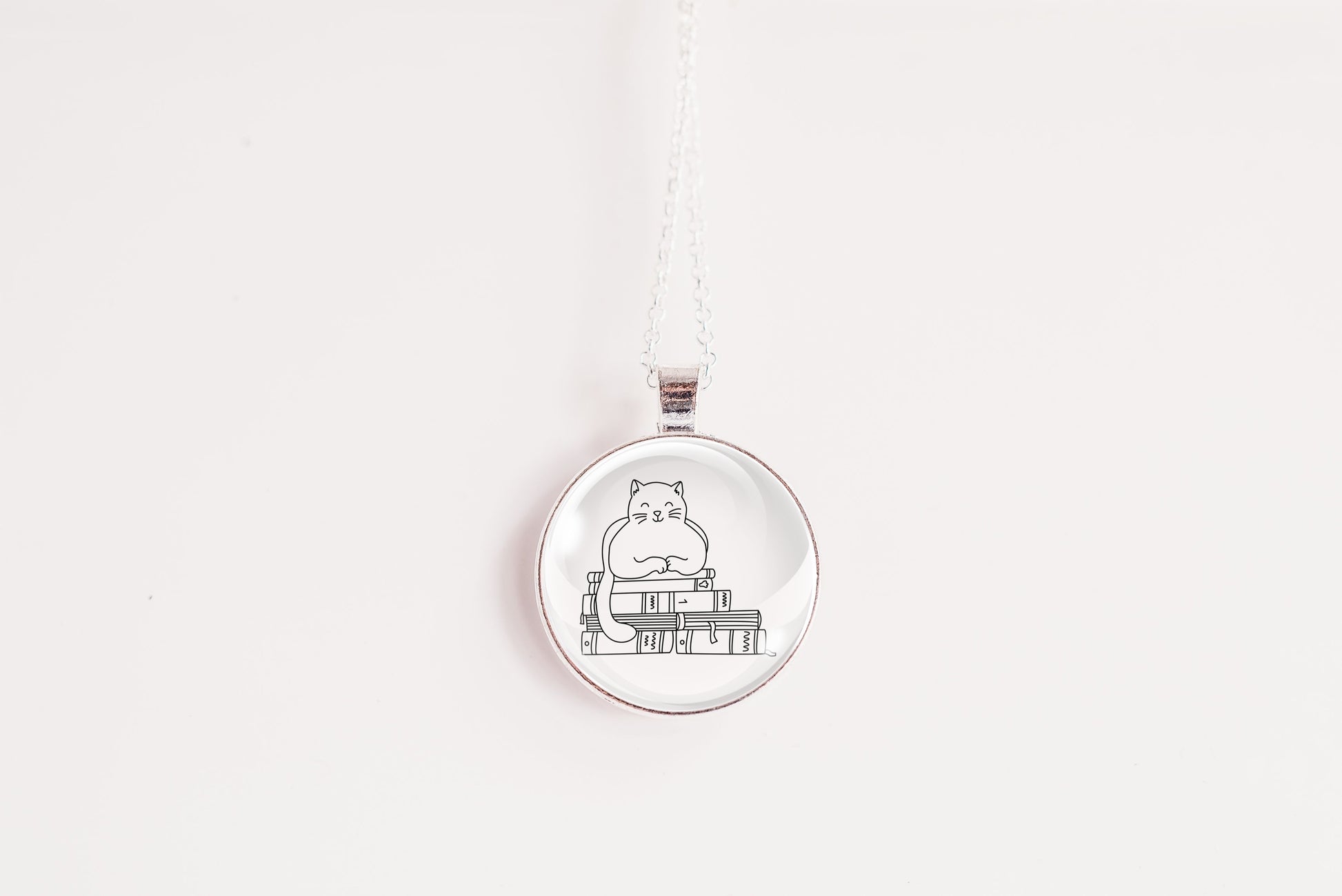 Glass cabochon pendant featuring a black line drawing of a cat sitting on stacked books
